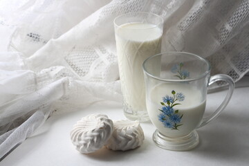 White glass and mug with milk and marshmallows on a background of white tulle