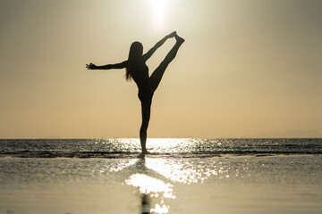 Silhouette of woman standing at yoga pose on the tropical beach during sunset. Girl practicing yoga near sea water