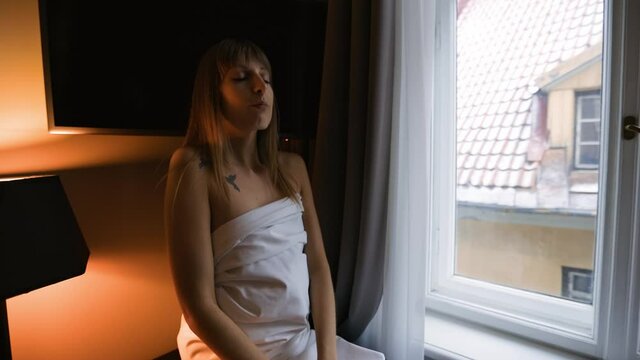 Sensual woman in bedsheet sitting on table doing breath meditation