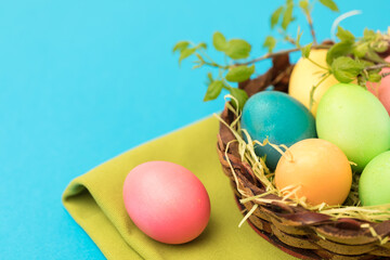 Easter painted in bright colors eggs in a decorative basket. Decorated with a green twig, a napkin.