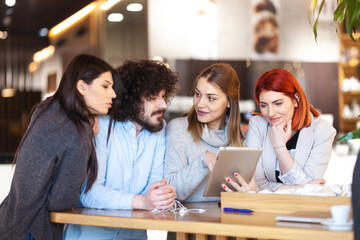 Four friends sitting at a cafe bar looking at tablet. Positive and smiling face expressions.
