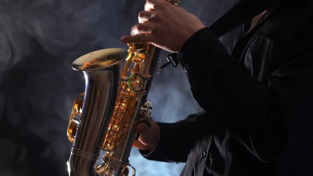 Closeup of hands playing on saxophone isolated on smoked background 