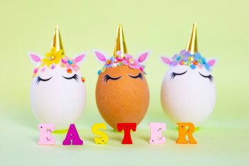 Fototapeta premium brown and white Easter eggs decorated in the form of unicorns and wooden letters Easter on a green and yellow background, a minimal creative concept of a happy Easter