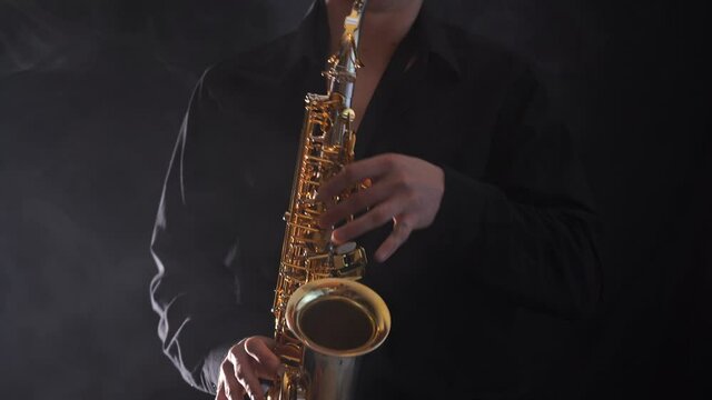 Closeup of hands playing on saxophone isolated on smoked background 