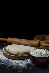 Dough on a dark background. Rolling pin on home test on a black background. Floured dough, tools for working with dough for baking are laid around the dough.