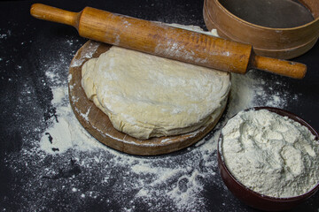 Dough on a dark background. Rolling pin on home test on a black background. Floured dough, tools...