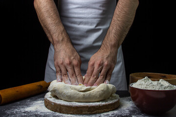 Dough on a dark background. Male hands knead the dough. Chef working with dough on black background