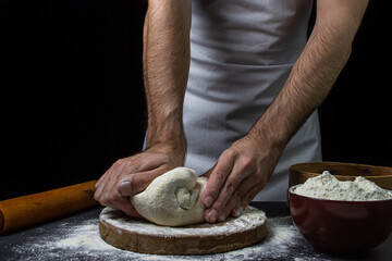 Dough on a dark background. Male hands knead the dough. Chef working with dough on black background