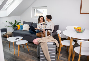 Smiling couple sitting on sofa using laptop in hotel room.