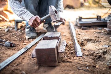 Closeup hands of a blacksmith hits iron or steel sheet with a hammer at a workshop outdoors.
