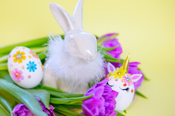 Easter Bunny, white Easter eggs decorated in the form of unicorns and tulips on yellow background, a minimal creative concept of a happy Easter