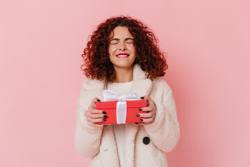Fototapeta premium Woman in joyful anticipation holds gift. Photo of lady with dark curly hair on pink background