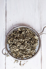 Dry raspberry leaves in a tea strainer close-up. Alternative herbal medicine. Healthy lifestyle concept. Composition with organic, natural herbal tea on a light wooden table.