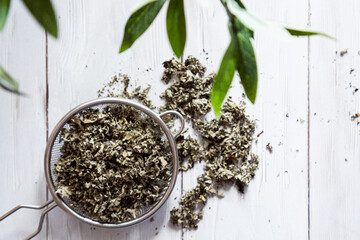 Dry raspberry leaves in a tea strainer close-up. Alternative herbal medicine. Healthy lifestyle concept. Composition with organic, natural herbal tea on a light wooden table.