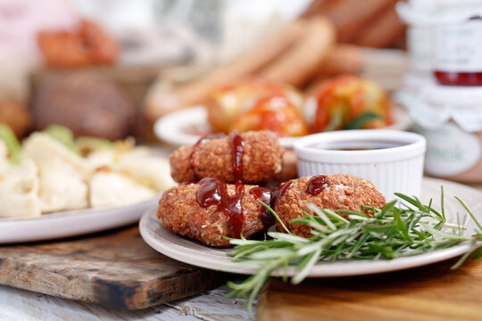 Close-up of fried chicken Kievs, poultry cutlets on a white plate, on a wood cutting board. De volaille, meat patties, burgers, minced cutlets served with bbq sauce, garnished with fresh rosemary.