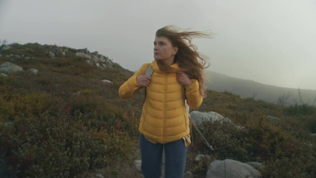 Beautiful cinematic shot of young woman in yellow tech puffy jacket walk in epic scenery during hike or exploration trip. Moody and inspirational travel wanderlust. Serious hike experience concept