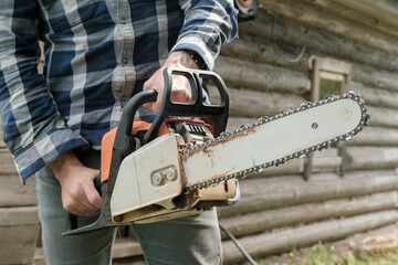 A man holds a professional chainsaw in his hands, he is ready to sawing firewood in the village.