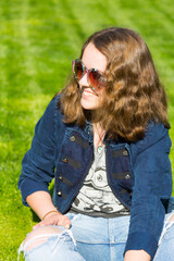 Lächelndes Mädchen mit Retro Sonnenbrille sitzt auf dem Rasen, Teenager, Portrait