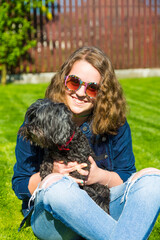 Junges Mädchen mit Retro Sonnenbrille hält ihren schwarzen Bichon Hund auf dem Arm
