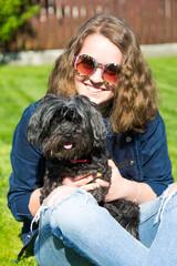 Junges Mädchen mit Retro Sonnenbrille hält ihren schwarzen Bichon Hund auf dem Arm