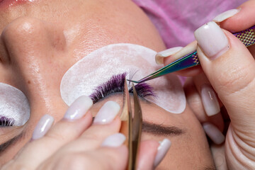 Eyelash Extension Treatment with tweezers. Woman Eyes with long purple extended lashes