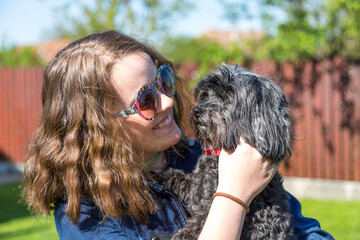 Junges Mädchen mit Retro Sonnenbrille hält ihren schwarzen Bichon Hund auf dem Arm