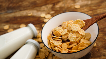Healthy cornflakes and milk and a wooden spoon on wooden table.