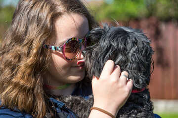 Junges Mädchen mit Retro Sonnenbrille hält ihren schwarzen Bichon Hund auf dem Arm