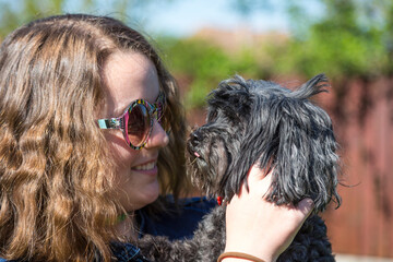 Junges Mädchen mit Retro Sonnenbrille hält ihren schwarzen Bichon Hund auf dem Arm