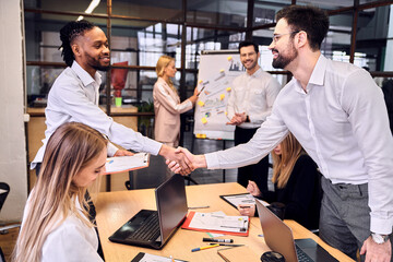 Modern businessmen shaking hands while working together with their team in the board room