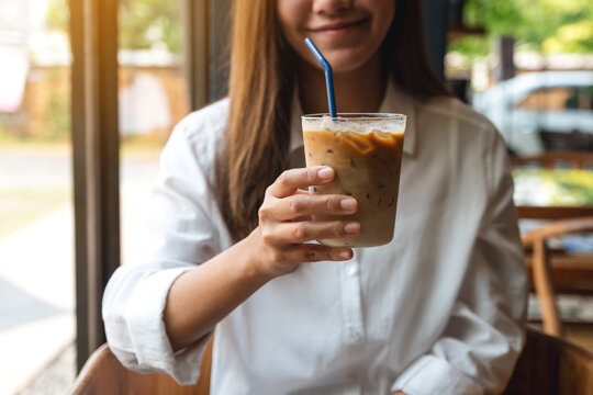 Closeup image of a beautiful young asian woman holding and showing a glass of iced coffee