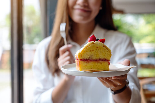 Closeup image of a beautiful young asian woman holding and eating a cake by fork