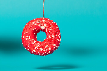 Donut on fishing hook on colored studio background. Concept calorie trap, delicious bait