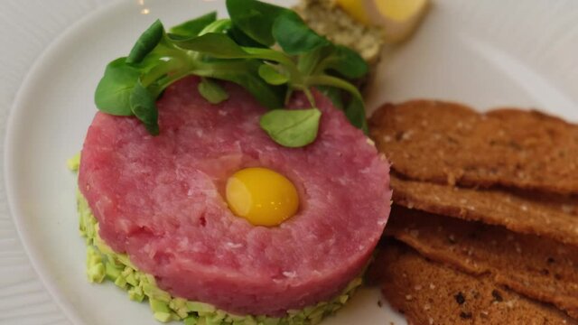 Close-up of fresh salmon with tuna and avocado tartare with caper salsa, pickled cucumbers and truffle oil in a cafe restaurant decorated by a chef.