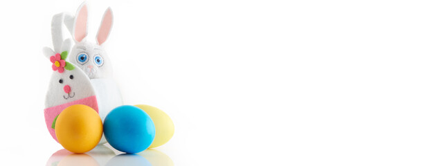 Fototapeta premium Banner with hand made white rabbit in basket and three colored eggs on white background.