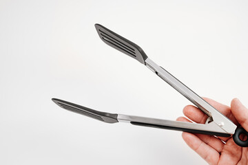 black Kitchen tongs in hands on a white background.