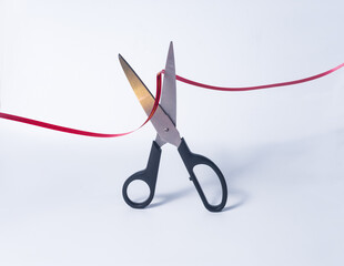 Metal scissors with a black plastic handle cut a colored ribbon on a light background