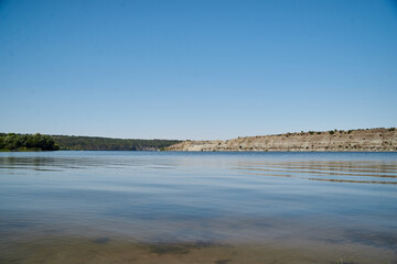 Scenic view over wide river and it's bank. Beautiful natural countryside landscape with blue sunny sky. Summer getaway vacation into isolated places. Calm water - perfect for meditation.
