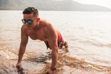 A buff asian man wearing shades does pushups at the beach. Chest workout or calisthenics outdoors.