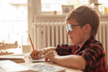 Nerdy boy writing in a notebook during home schooling in the living room.