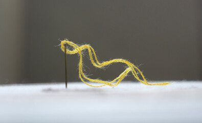 Sewing needle with yellow thread on a gray background. Macrophoto in trend colors of 2021