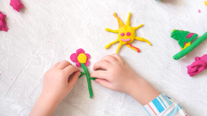 Hands of little girl making flower and sun and other  from colorful clay dough, plasticine, Home Education game with clay. Early development concept