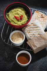 Shawarma with meat and vegetable filling and dips on a metal cooling rack, studio shot on a dark brown stone surface
