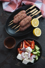 Fresh uncooked lamb kofta kebabs and greek salad over brown stone background, vertical shot, top view