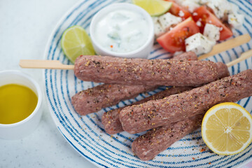 Blue and white plate with fresh uncooked kefta kabobs made of beef and lamb meat, selective focus, studio shot