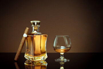 close up view of cigar, bottle of cognac and a glass aside on brown back. 