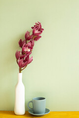 Coffee cup and vase of cymbidium flowers on wooden table. green background - obrazy, fototapety, plakaty