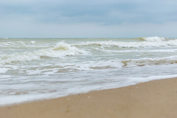 Seashore in cloudy weather. Waves with foam on the water.