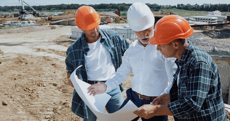 engineer and builders talking and looking at blueprint on construction site
