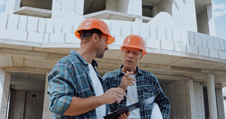 Builders looking at clipboard while talking on construction site